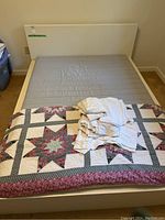 Double platform bed with light-colored frame and bedding including quilt and sheets
