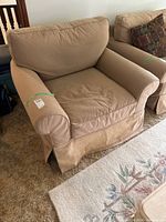 Front angle view of beige Restoration Hardware slipcover armchair showing overall condition with stains and faded fabric.