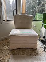 Full front view of beige upholstered slipper chair with button tufting and tailored skirt, showing overall condition.