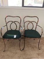 Front view of two metal armchairs with green padded seats placed on carpet near window.
