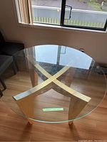 Top view photo of the round glass dining table showing clear glass surface and X-shaped wood and metal base beneath.
