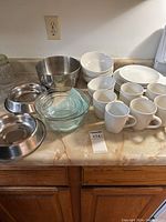 Overview of mismatched white dishes, glass bowls, metal mixing bowl, and metal dog dishes arranged on a counter.