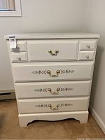 Front view of white dresser with four drawers and floral design on three bottom drawers.