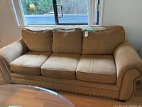 Full front view of a light brown fabric couch with three cushions in a room by a window.