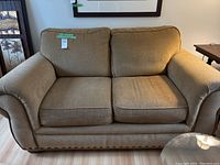 Front view of light brown fabric loveseat showing two seat and back cushions, rolled arms, and piping detail. Some fabric wear visible.