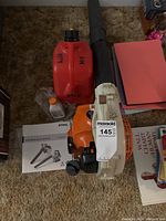 Handheld blower, manual, fuel can and oil bottle on carpet