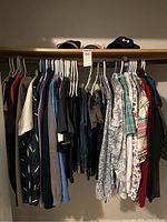 Wide view of multiple men's shirts and pants on hangers on a closet rack.