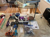 Overview of desk surface showing multiple pairs of scissors, tape dispenser with rolls, purple desk lamp, plastic container with small items and lighters.
