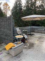 Photo capturing entire lot setup on a concrete patio with umbrella, screen, chairs, table, and storage bin with shovel.