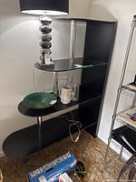 Shelving unit with graduated oval shelves and metal rods, containing a lamp, green decorative plate, and glassware