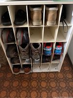 Front view of white shoe rack with 15 compartments filled with various men's shoes including athletic, casual, boots and sneakers.