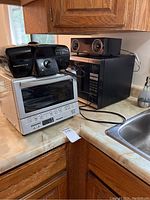 Photo showing four appliances on kitchen counter: Panasonic toaster oven, microwave, Hamilton Beach sandwich maker, and Samsung Bluetooth speaker