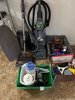Photo showing Kenmore vacuum cleaner with hose and attachments standing next to a grey portable ironing board and a grey bin with various cleaning and shoe care items.
