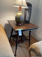Photo of the ornate wooden side table with ceramic lamp and portable fan placed on top, showing detailed legs and overall table shape.