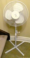 White 18 inch oscillating fan on adjustable stand next to wall and staircase.