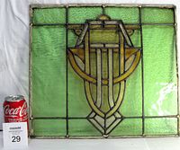 Full front view of the antique stained glass window with a comparison Coca-Cola can and MaxSold label for scale. Shows the green and amber glass panels with old lead caming.