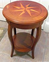 Round wooden side or end table showing inlaid star design on tabletop, curved legs, and lower shelf.