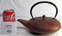 Side view of reddish-brown cast iron Japanese teapot with black handle and dragon motif, next to soda can for scale.