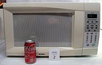Front view showing the full microwave with door and control panel, measured against a soda can for scale.