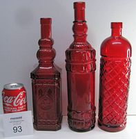Three red glass decorative bottles with varying heights and embossed patterns, shown next to a can for scale.
