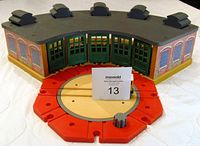 Overall view of Thomas The Tank Engine wooden roundhouse storage building placed on a white surface, showing red track splitter in front with no engine.