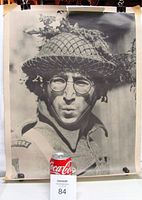 Full view of the vintage black and white John Lennon poster, shown with a Coca-Cola can for scale. Visible clips holding the poster and tape residue on corners.