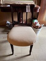 Front view of an antique wooden chair with a beige upholstered seat and carved vertical slats on the backrest.