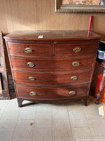 Front view of antique mahogany dresser showing curved drawer fronts and brass oval handles