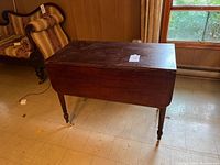Photo of the solid mahogany drop leaf table, side view with leaves down, showing the entire table and tapered legs with brass casters.