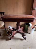 Side view of antique wooden games table showing pedestal base with claw feet.