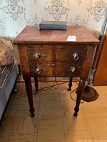 Side view of antique solid mahogany side table showing two drawers with metal ring pulls and turned legs.