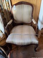 Front view of the wood-framed armchair showing the striped beige upholstery, carved floral accents on crest rail and legs, and padded armrests.