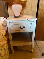 Front view of white wooden bedside table showing drawer, open shelf, and curved legs.