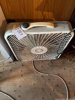 Photo of a used white Master BDR box fan on wooden surface showing front with protective grill, carry handle, and power cord.