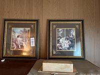 Two framed cherub prints displayed side by side against wood panel wall.