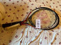 Photo of two children's tennis racquets on a floral patterned bed sheet, one with 'Wimbledon' on the strings and both racquets showing wear on grips.
