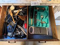 Two open kitchen drawers showing assortment of cutlery, kitchen utensils, and serving tools