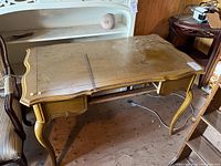 Wooden desk painted yellow, showing wear, curved edges, and cabriole legs, saw placed on desktop.