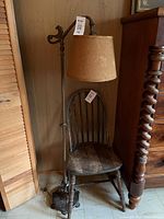 Photo showing full length of the 58-inch floor lamp with woven fabric shade and ornate dark metal stand, standing beside a wooden chair and furniture.