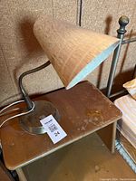 Photo showing the mid-century modern gooseneck desk lamp with metallic cone-shaped shade on wooden side table, visible cord and weighted circular base with wear marks.