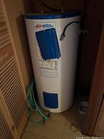 Photo of a white John Wood hot water heater with blue panels, set in a corner next to a wooden louvre door.