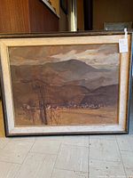 Framed landscape painting of mountains, fields, trees, and village in muted earth tones.
