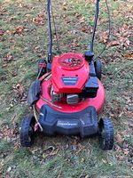 Front view of red PowerSmart lawn mower on grass with fallen leaves, showing engine, deck, handle, and wheels.