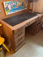 Solid wood desk showing the left side with five drawers and the black leather top surface.