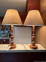 Two Mid-Century Modern style wooden table lamps with beige cone-shaped fabric shades placed side by side on a tabletop.