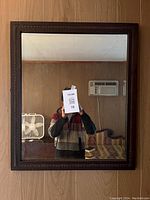 Full view of rectangular mirror showing wooden frame, reflection of room behind camera.