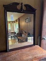 Front view of the framed wall mirror showing the reflective surface and decorative curved top with finial.