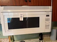 White Panasonic microwave oven mounted above stove, showing front with black window and control panel with buttons on the right.