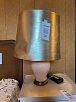 Photo showing pink porcelain lamp with a gold fabric shade that has a noticeable dent on one side.