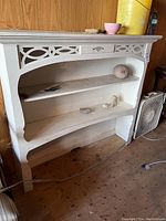 Front view of white wooden shelf hutch with decorative cutouts and displayed objects